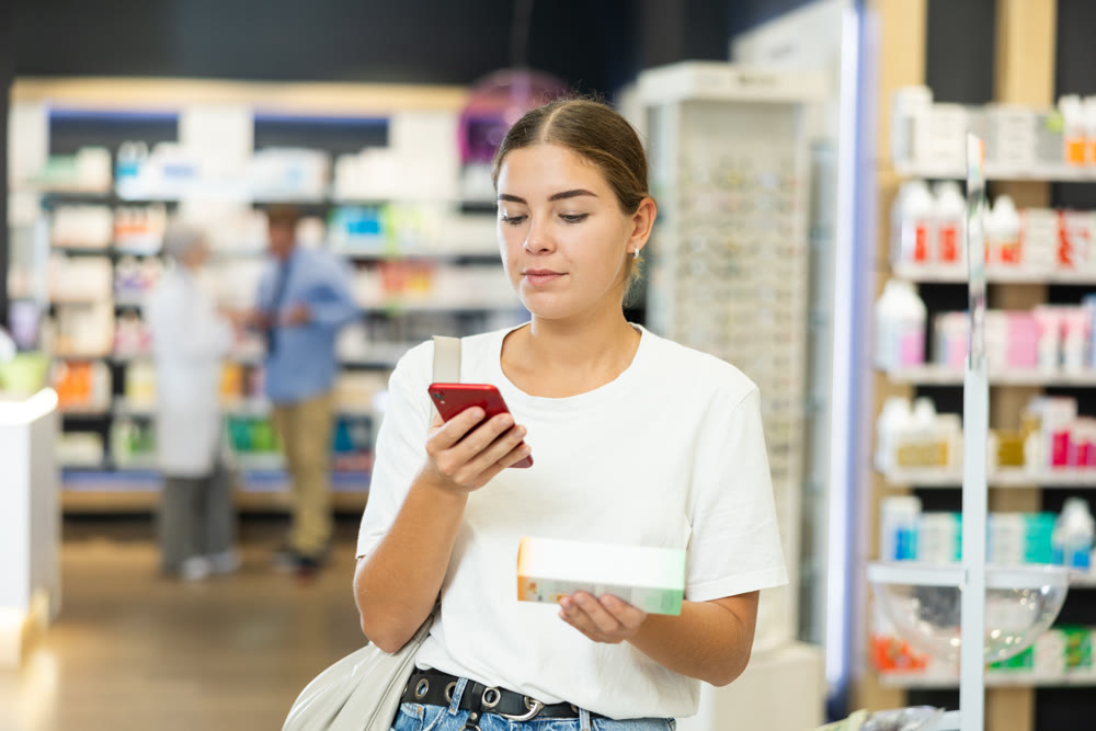 Woman scanning barcode on cosmetics package with her phone in pharmacy. Searching for information via Internet