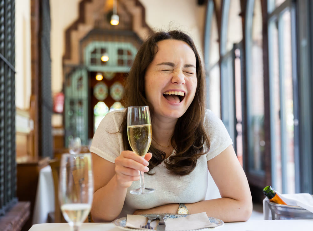 Laughing woman with glass of wine at table in restaurant