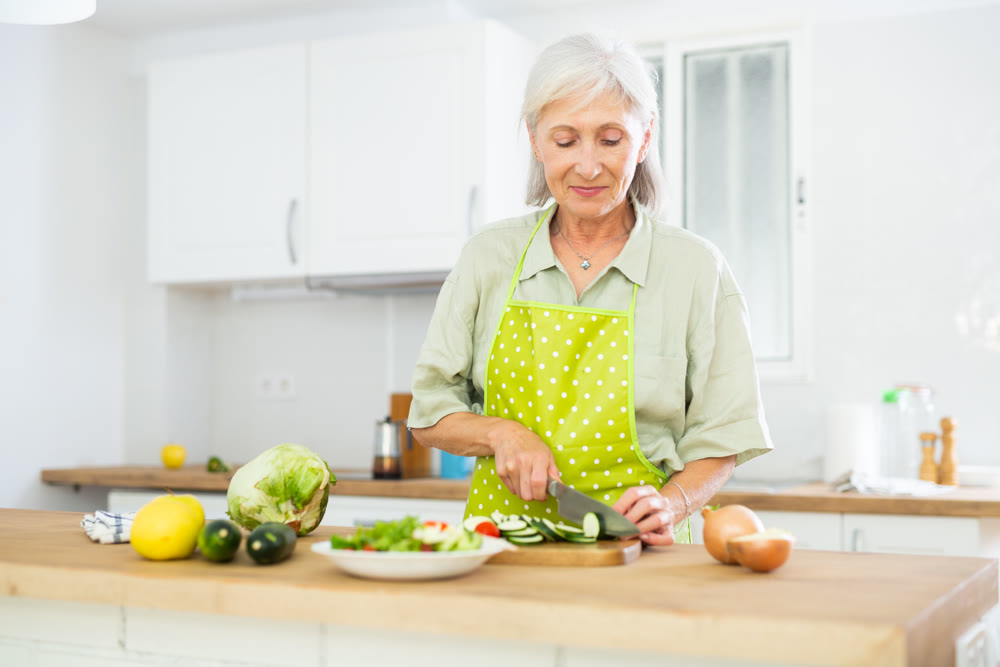 Cheerful elderly woman cooking salad at home