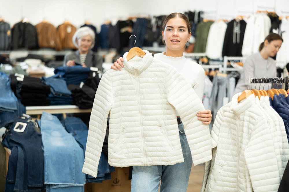 Young girl choosing white jacket in clothing store