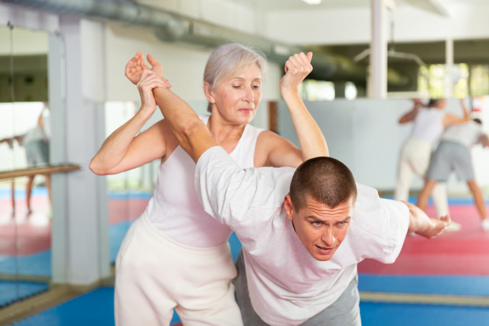 Elderly woman performing elbow strike and wristlock to man in self defense training
