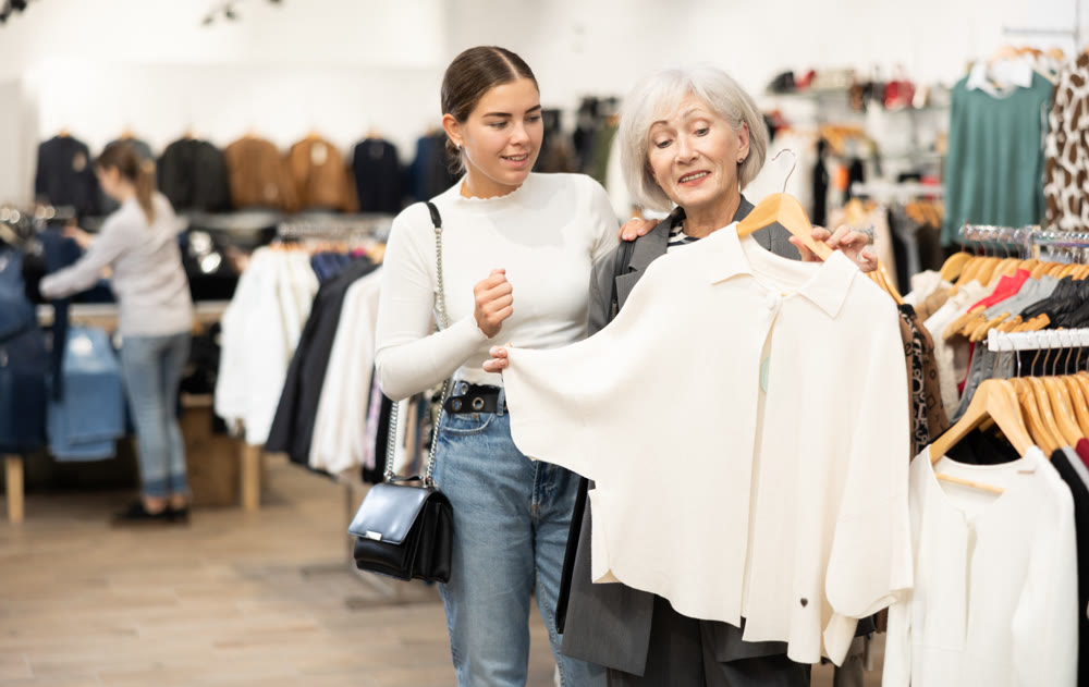 Young and old women customers looking at white cardigan in clothing store
