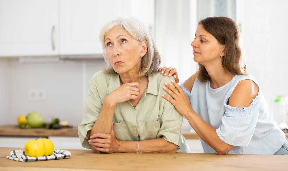 Apologetic adult daughter asking for forgiveness from her upset elderly mother after home disagreements