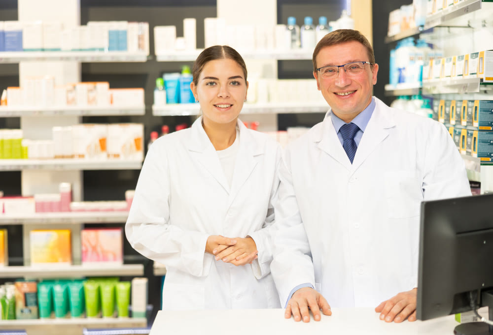 Young girl and middle-aged man pharmacists posing together in chemist's shop