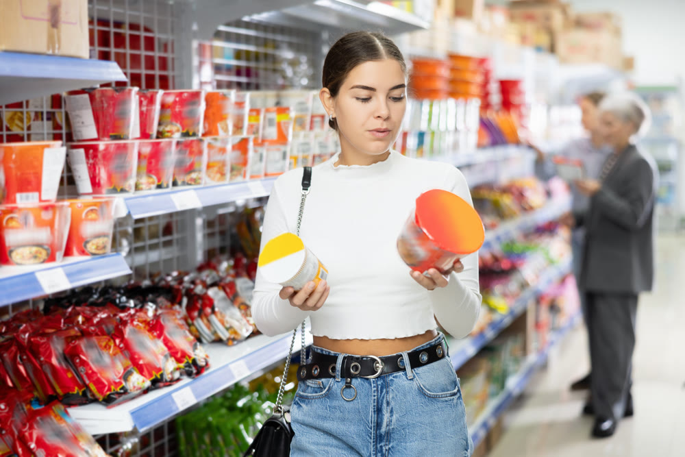 Young girl reading labels on cups of Asian instant noodles in store