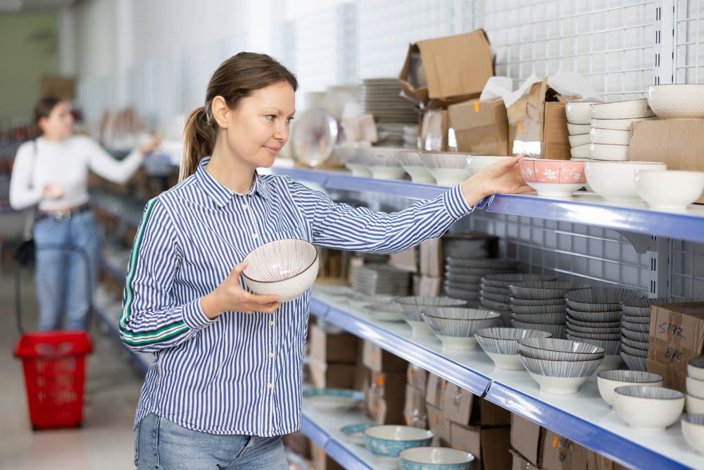Female shopper choosing ceramic bowls on shelves at Asian store