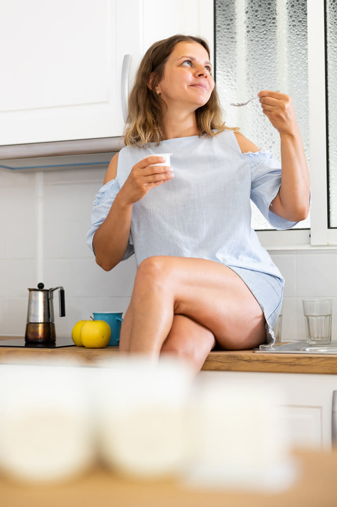 Young woman eating tasty yogurt in kitchen