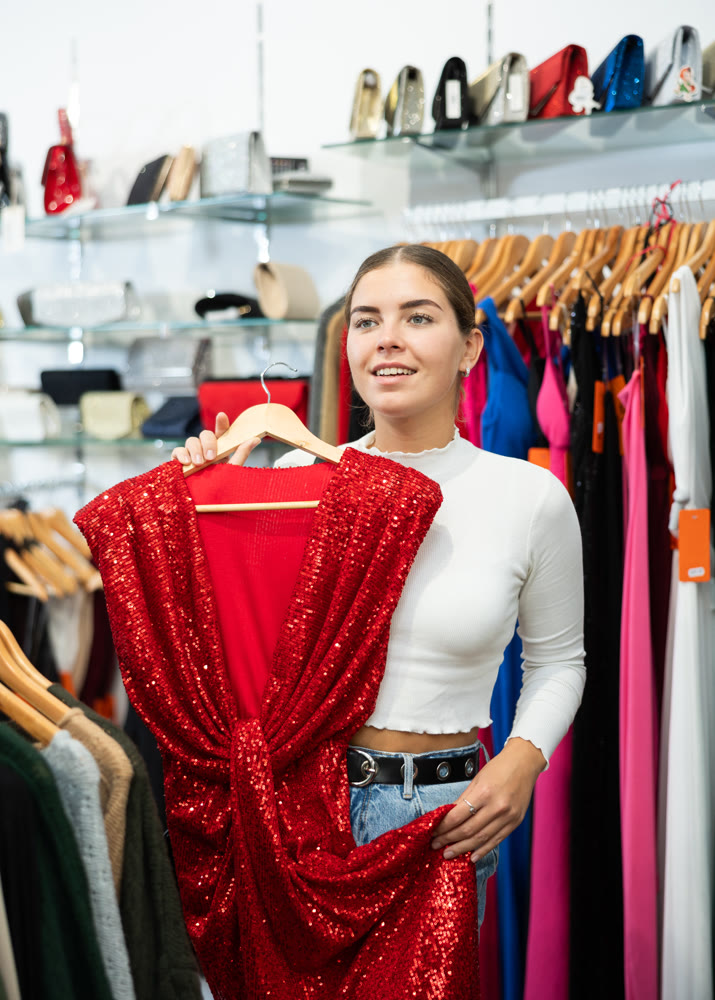 Smiling girl choosing colorful clothes in dressing room in showroom
