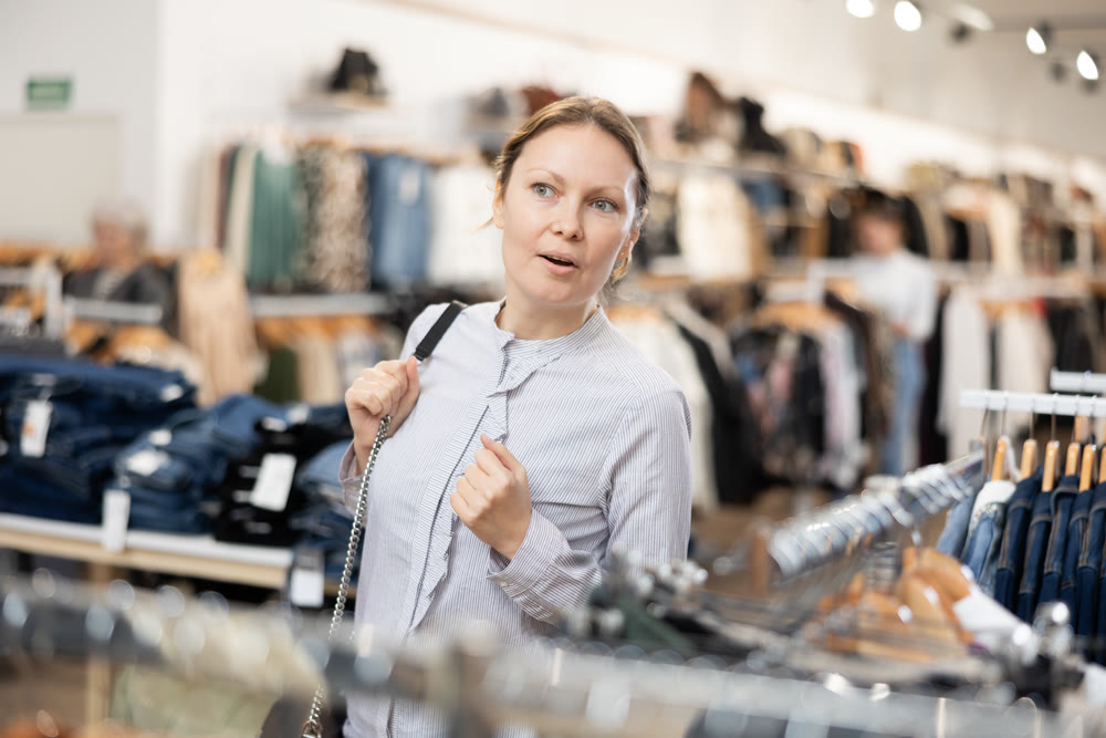 Portrait of joyful woman looking for fashionable clothes in clothing boutique