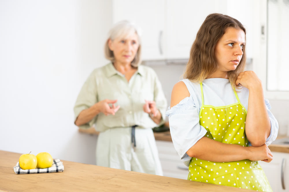 Senior woman scolding her adult daughter cooking breakfast in modern kitchen