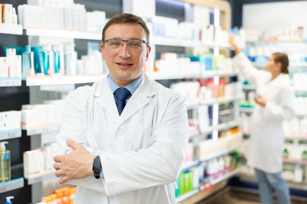Middle-aged male pharmacist posing in chemist's shop with large assortment