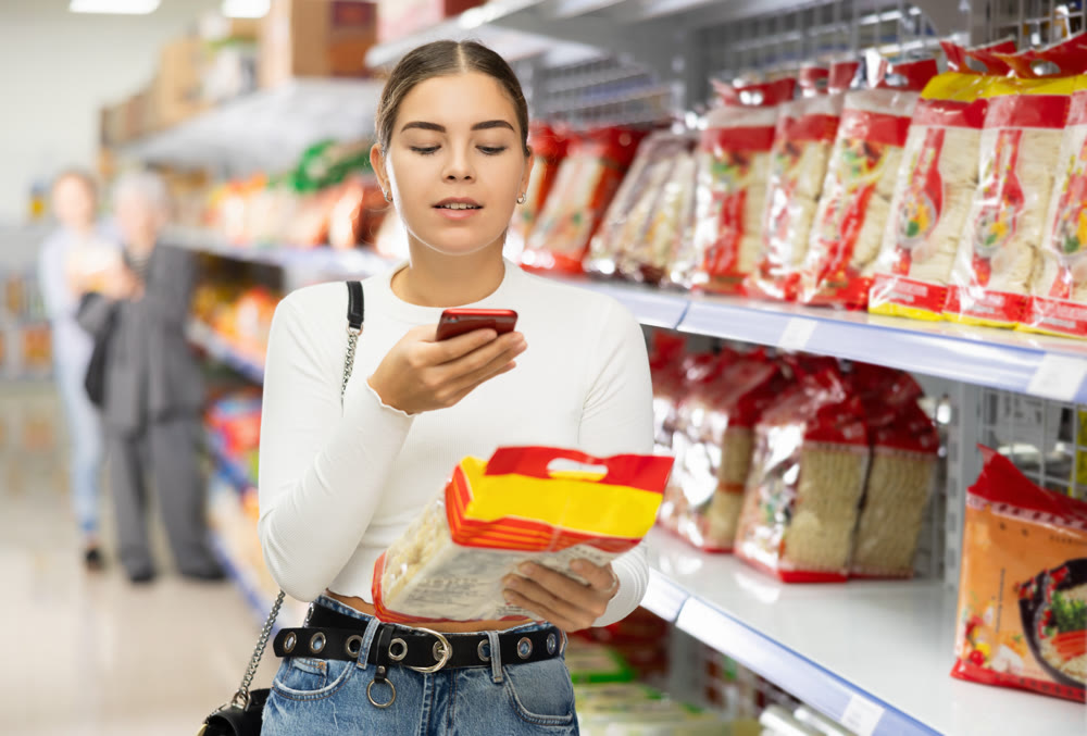 Young girl scanning QR code on noodle package with smartphone at store
