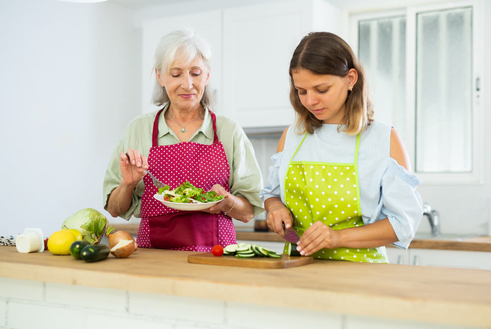 Senior woman and her adult daughter cooking salad together