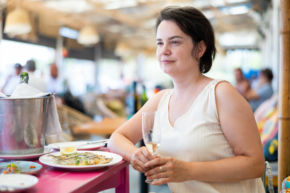 Woman relaxes on terrace of summer cafe and eats grilled sardines