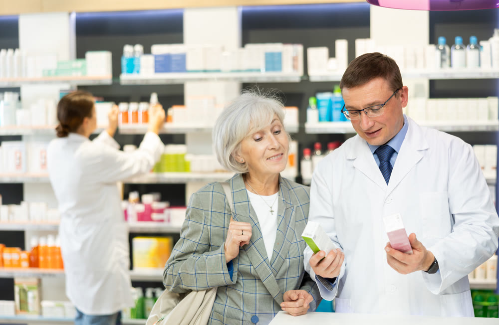 Middle-aged male pharmacist consulting old woman costumer about care product in box