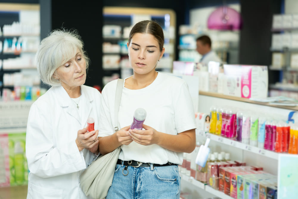 Girl buyer and an elderly woman pharmacist select intimate hygiene items together in pharmacy