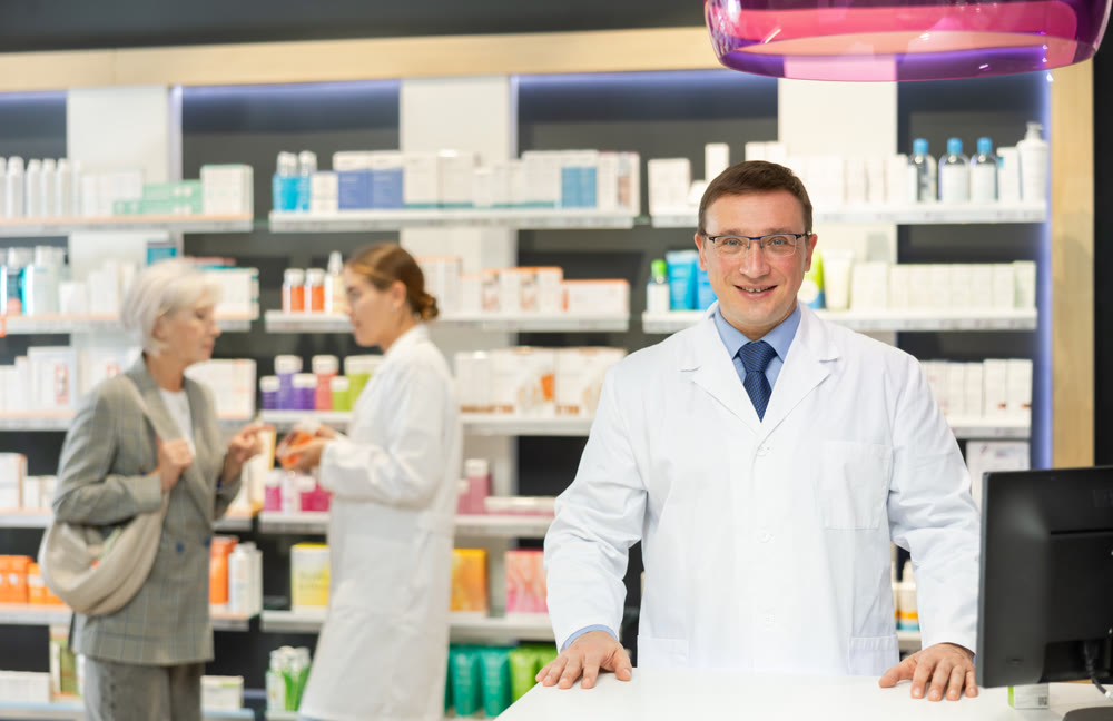 Portrait of friendly male pharmacist in a white coat against the background of a display case with medicines in pharmacy