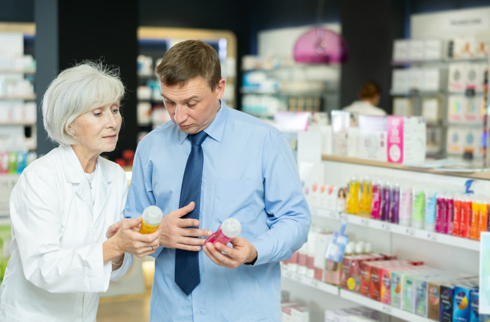 Senior woman pharmacist helps man buyer to decide on choice of lubricant.