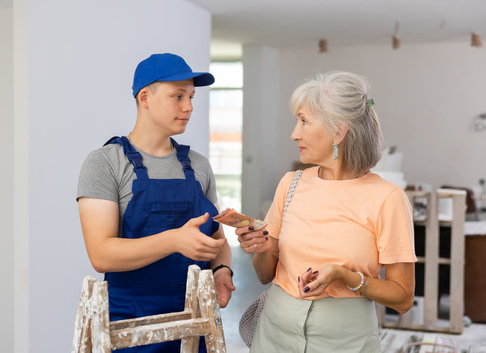 Senior woman paying wage to teenage boy assistant in construction site
