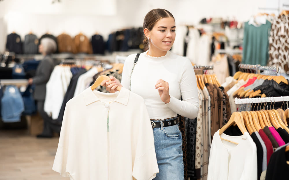 Young girl choosing white cardigan in clothing store