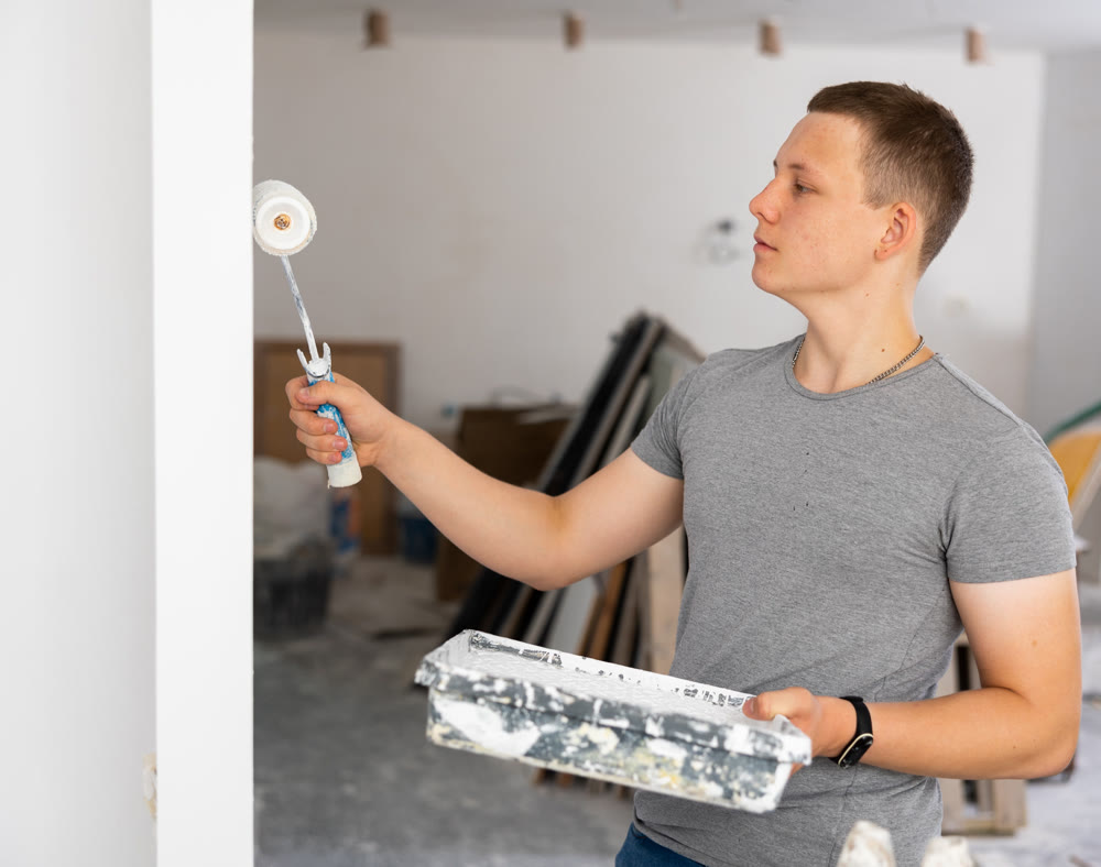Fifteen-year-old worker paints a wall with a roller
