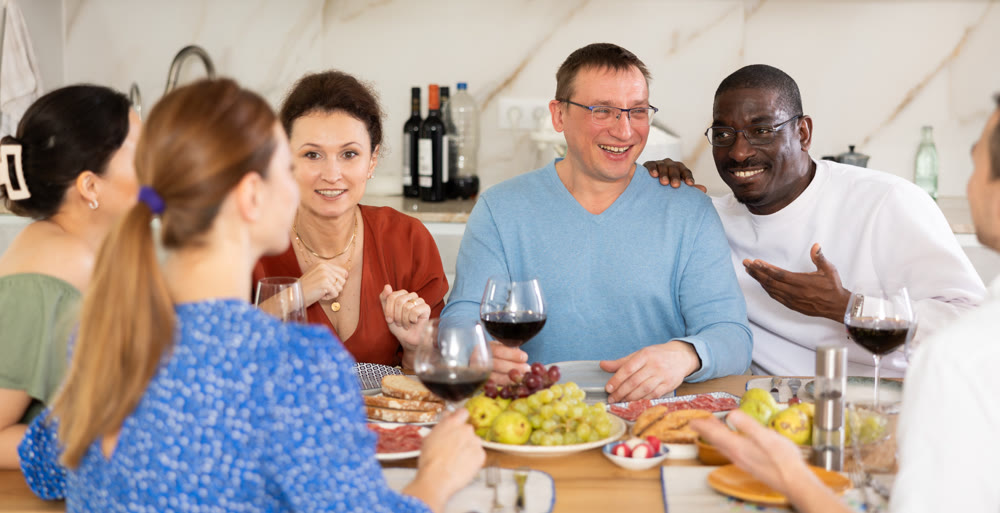 Cheerful adult friends dining and chatting in home kitchen