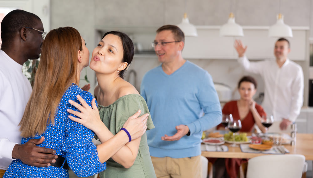 Asian woman greetingly kissing female friend at dinner party