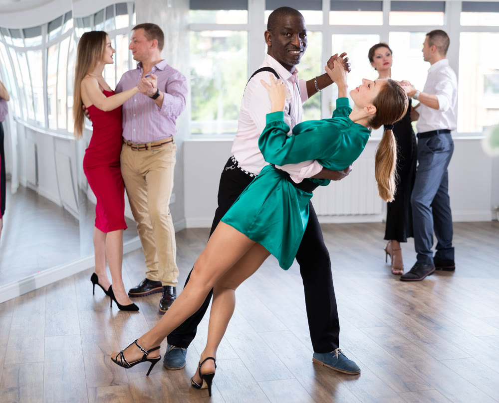 Elegant african american man performing kizomba paired with attractive woman in red in studio class setting