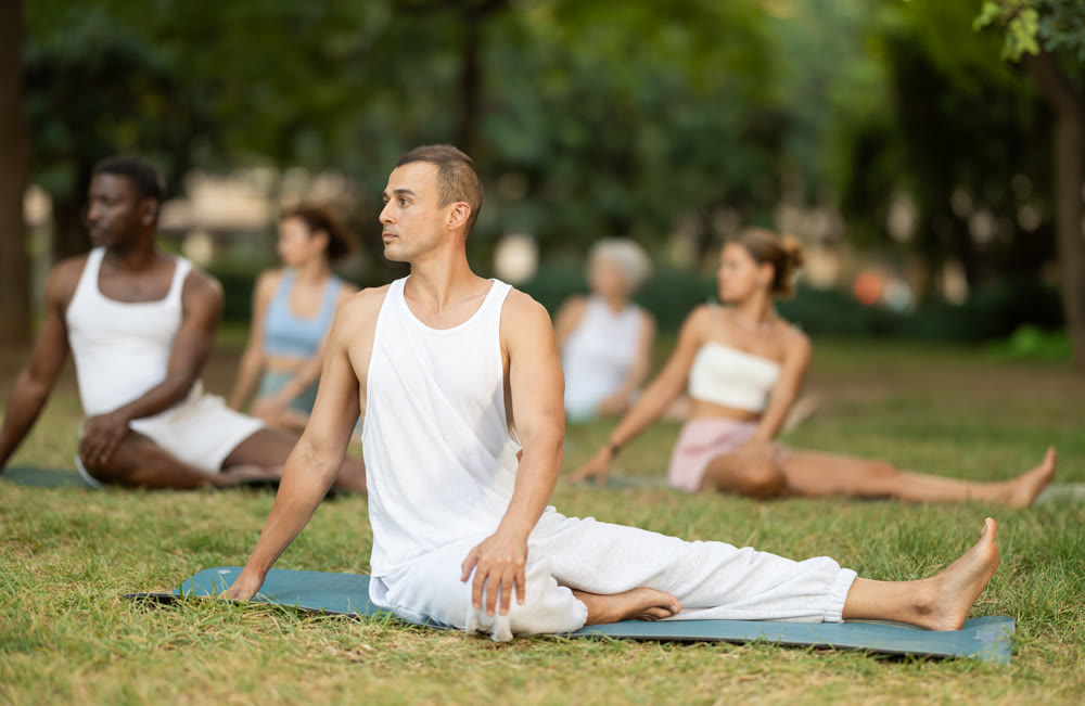 Athletic men and women of different nationalities warm up together before doing yoga in summer park