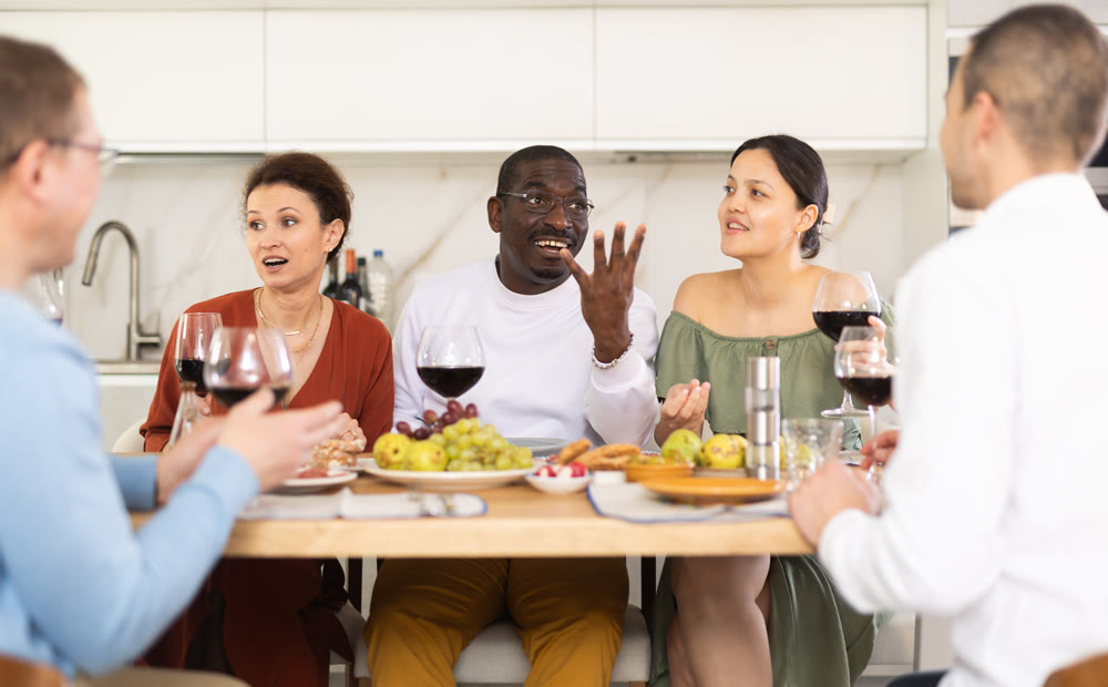Middle-aged friends sitting at table with a glass of wine while having friendly conversation