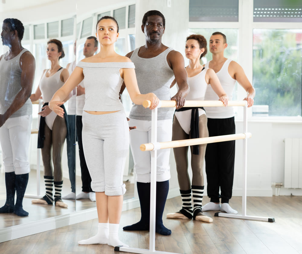 Group of dancers stand in first position at barre