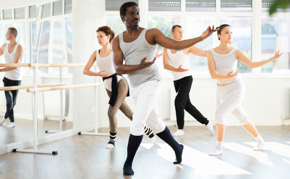 Group of men and women of different nationalities rehearsing ballet movements in studio