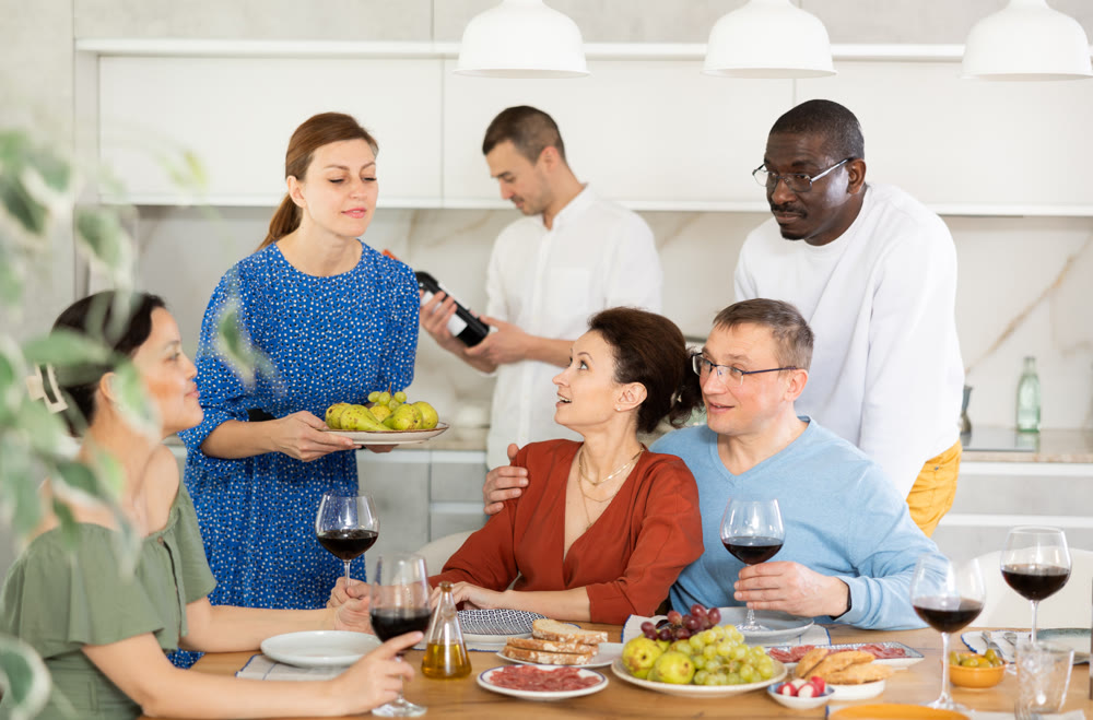 Happy middle-aged friends drinking wine and having friendly conversation around the table