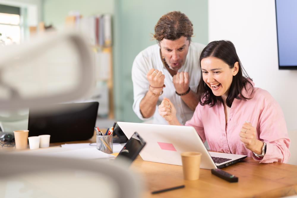 Happy colleagues sharing success while looking at laptop screen