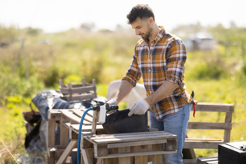 Young man filling bucket with water for field irrigation