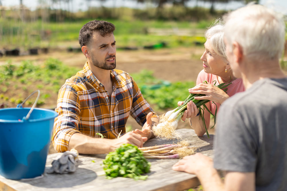 Young man and elderly couple sitting at table with harvest on field