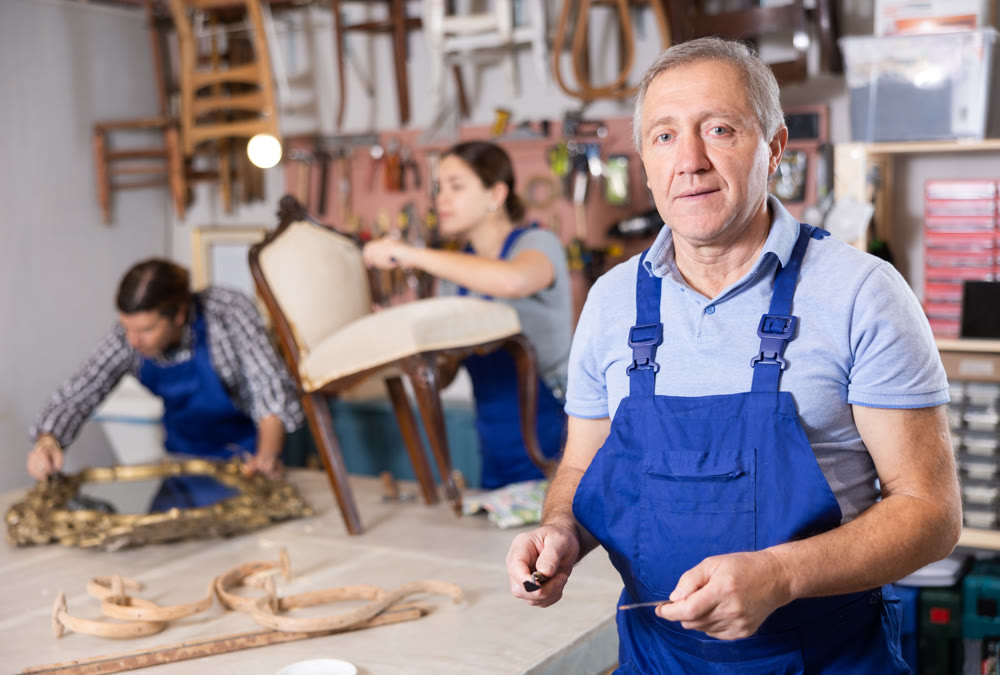 Confident successful craftsman restorer in uniform looking at camera in furniture repair woodwork shop