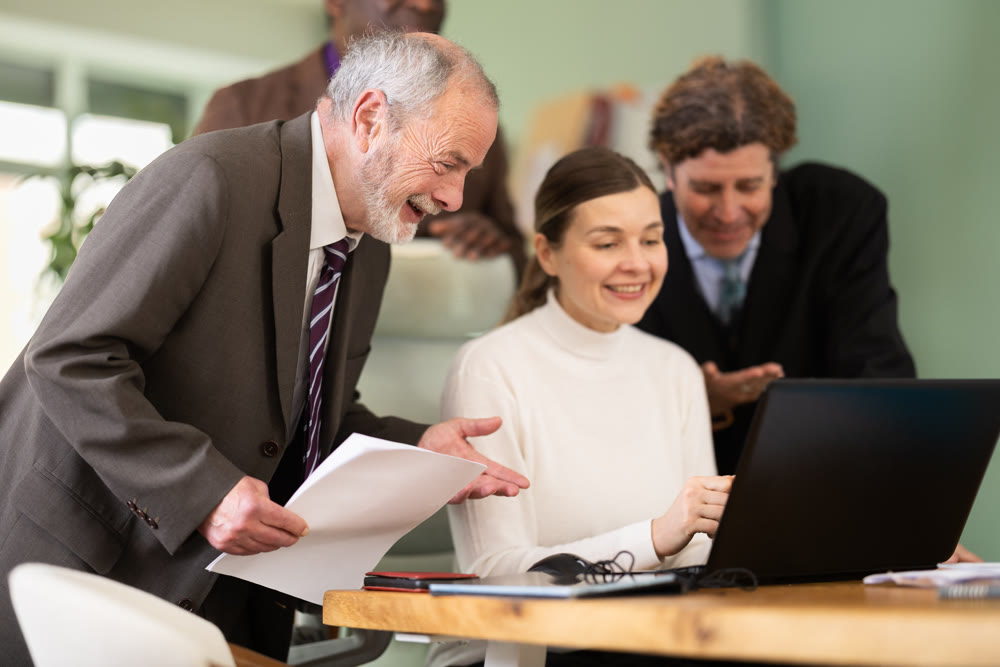 Team of businessmen laugh at funny video posted online during coffee break