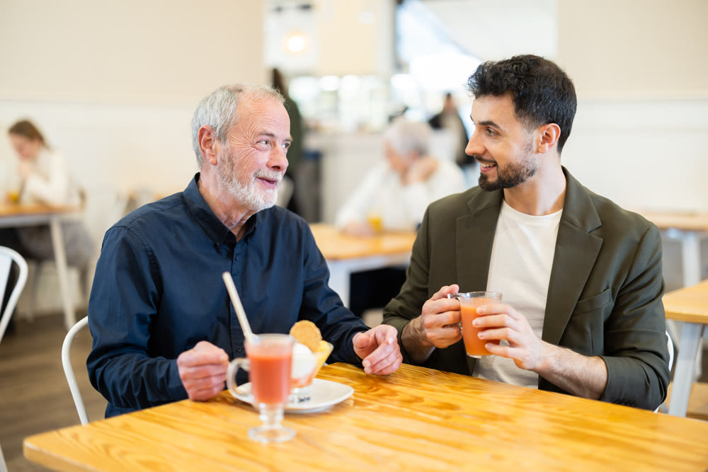 Two men are chatting at table in a cafe - eating ice cream and drinking juice