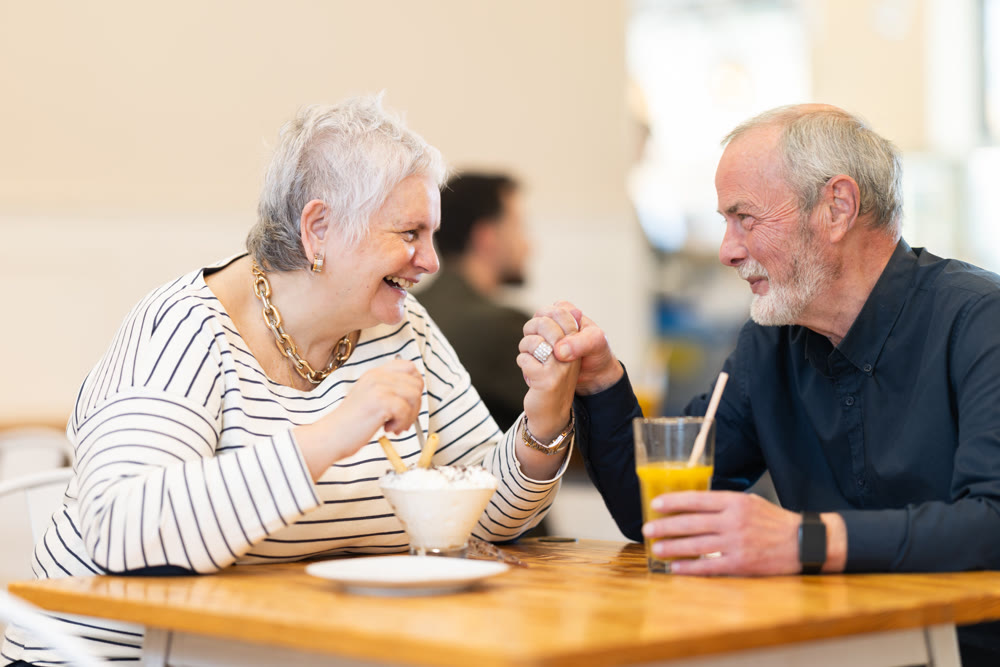 Elderly married couple are chatting happily with each other while sitting at table in a cafe and drinking juice and eat ice