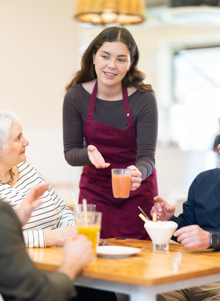 In restaurant hall, girl waiter brought order drink juice to senior family