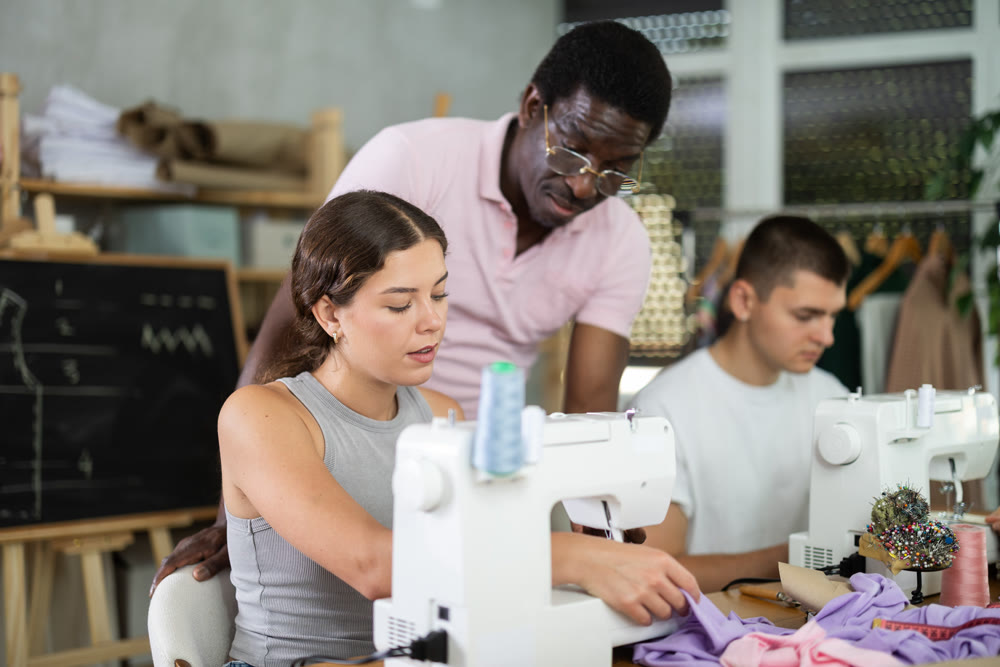 Middle-aged male teacher helping students sew