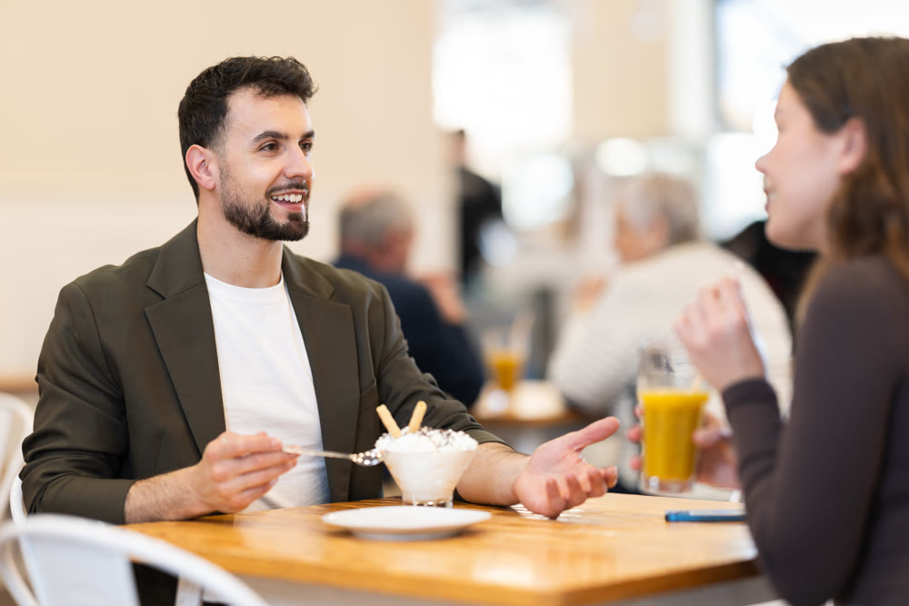 Positive couple are chatting happily with each other while sitting at table in a cafe and drinking juice and eat ice