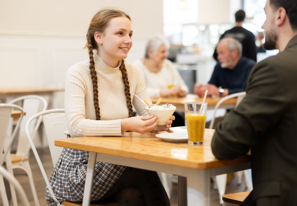 Mature father chats with his teenage daughter at a cafe table for breakfast with ice cream