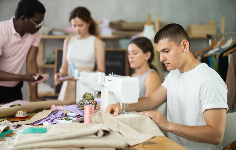 Engaged guy stitching fabric on machine in sewing class for adults