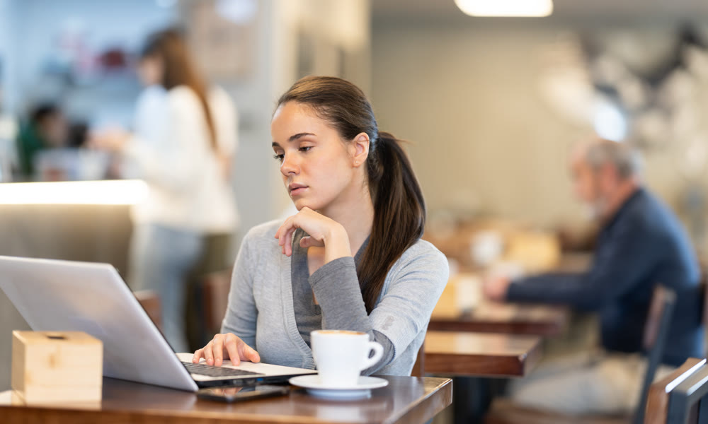 In cozy cafe hall, freelance young woman using laptop and drinks coffee.