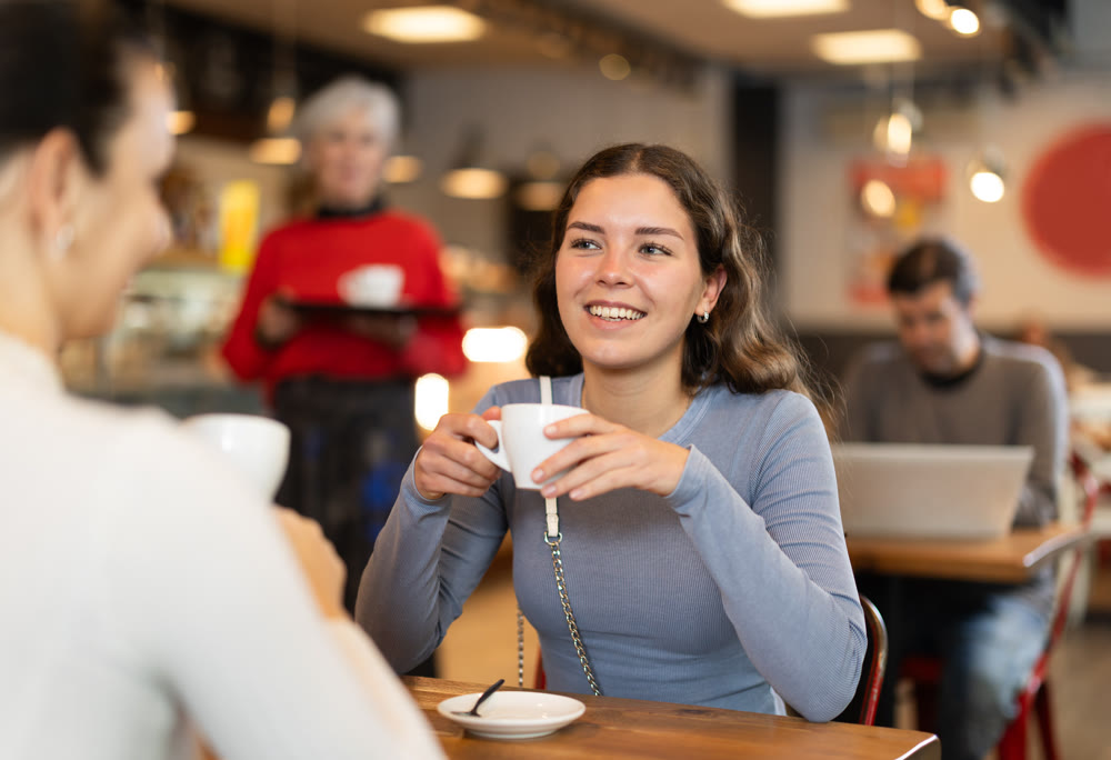 Girl in cafe sits opposite female companion, has nice conversation