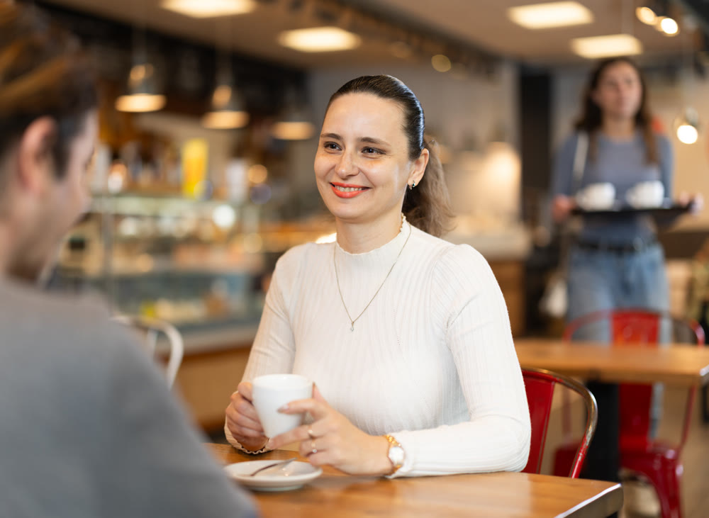 Woman in cafe sits opposite male companion, has nice conversation