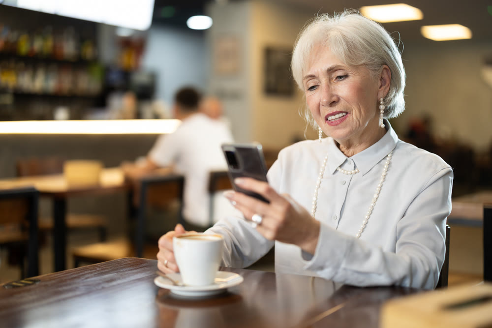 Senior woman in cafe drinks coffee and using mobile phone