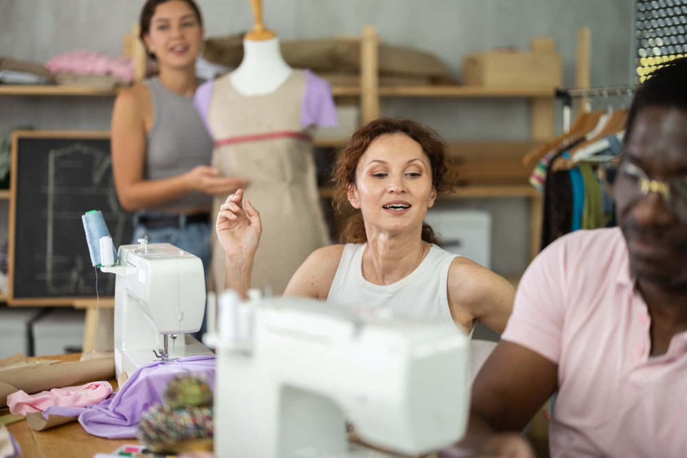Positive woman working at machine during group sewing course for adults